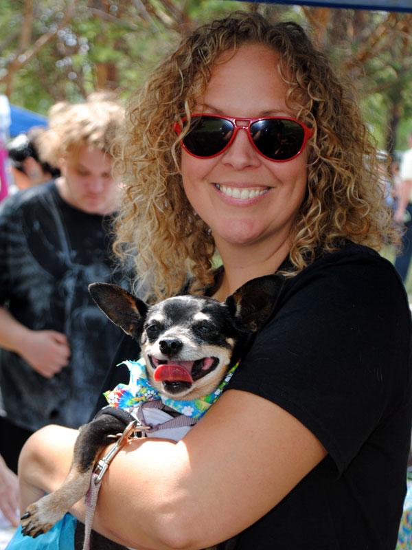 A woman with curly hair and red glasses holds a small black and white dog in her arms.