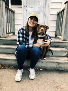 A woman wearing a black and white checkered shirt poses with a brown dog on concrete steps.