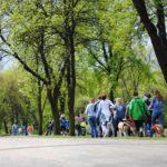 A large group of people stand in a park with their dogs.