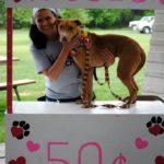 A woman holds a brown dog at a kissing booth