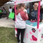 A woman wearing a hoodie holds a white dog at a kissing booth