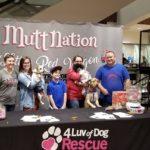 A group of volunteers stand in front of a Mutt Nation banner at a 4 Luv of Dog Rescue table