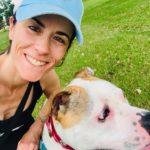 A woman with a blue cap smiles beside a white and brown pitbull