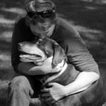A woman kisses the top of a dog's head.