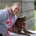A woman in a grey sweatshirt poses with a brown dog.