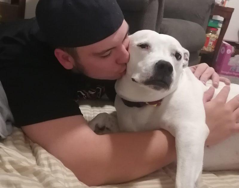 A man kisses the cheek of a white dog