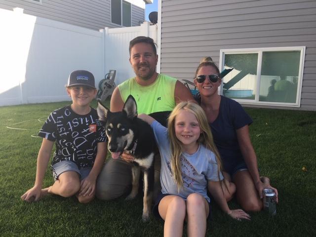 A man, woman, and two children sit with a black and tan dog with perky ears