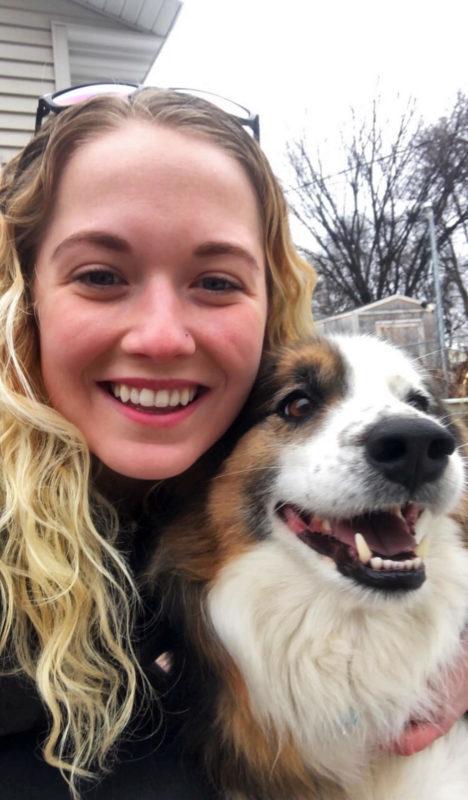 A woman poses with a white and brown dog. They are both smiling.