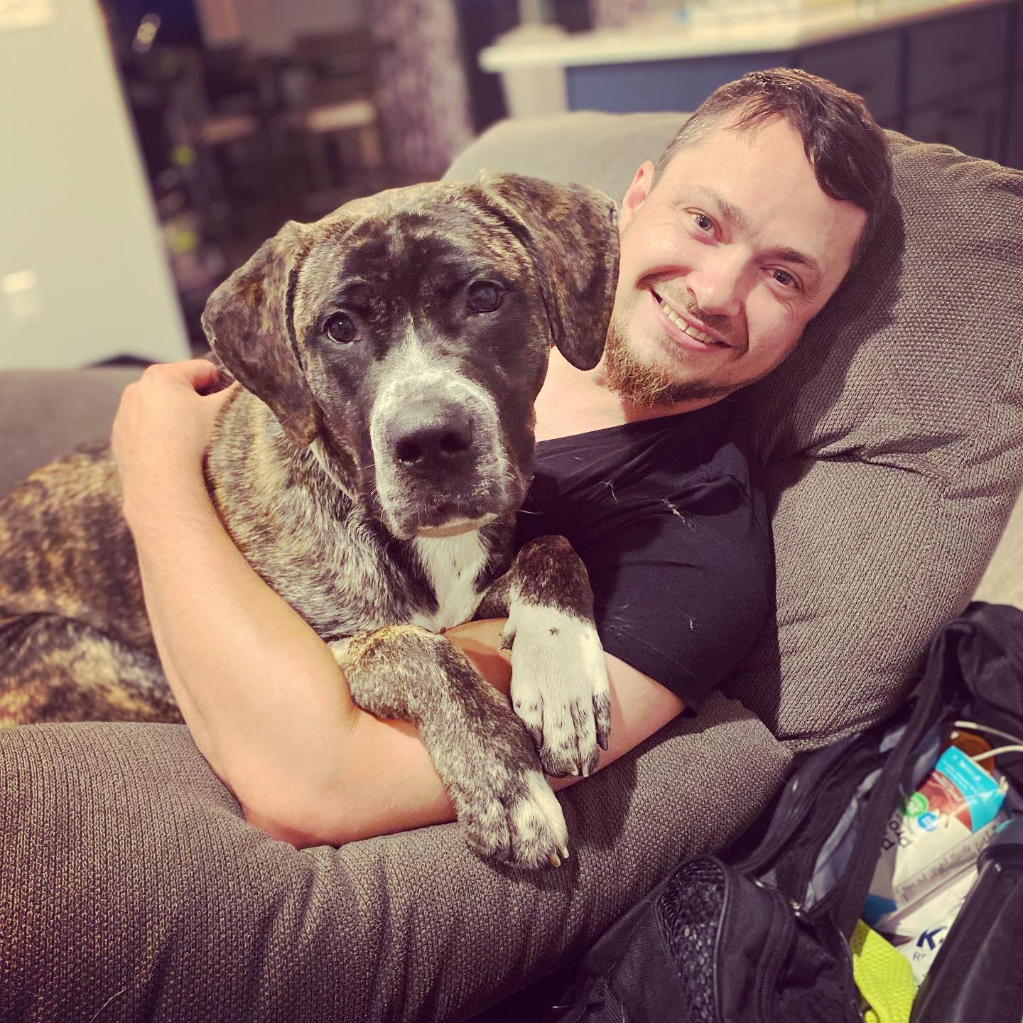 A man relaxes on a recliner with a big brown and white dog on his lap