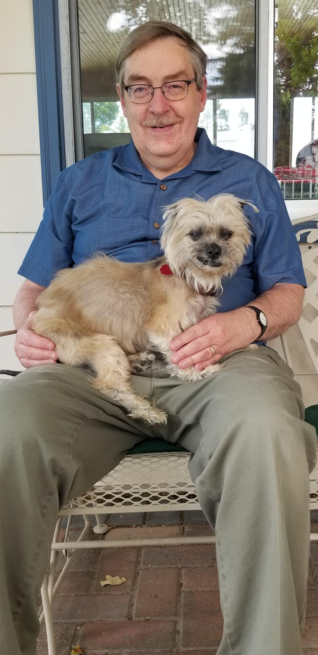A man holds a small brown dog in his lap.