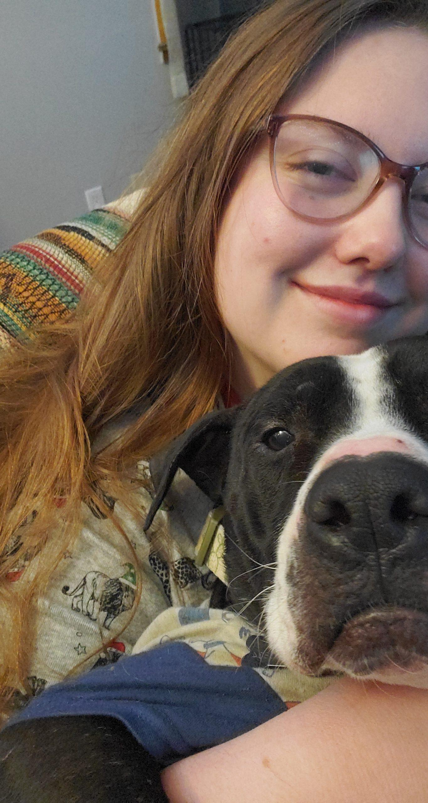 A woman takes a selfie with a black and white dog.