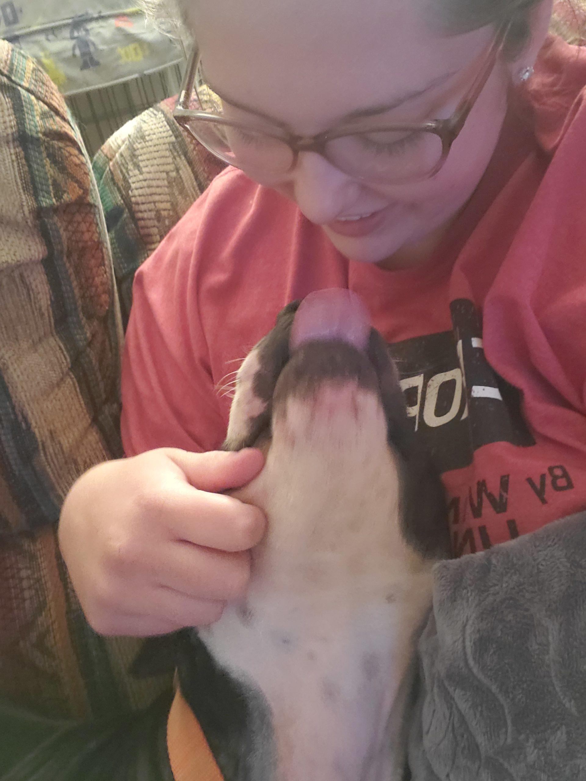 A dog is mid-lick, trying to slurp a woman's face.