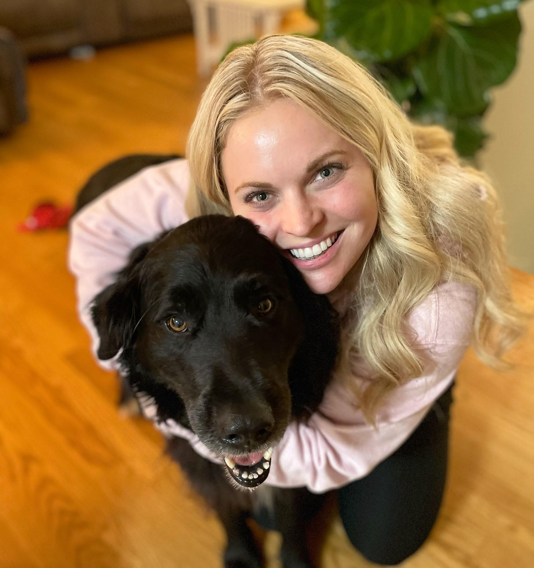 A woman smiles with a big black dog. Both are looking at the camera.