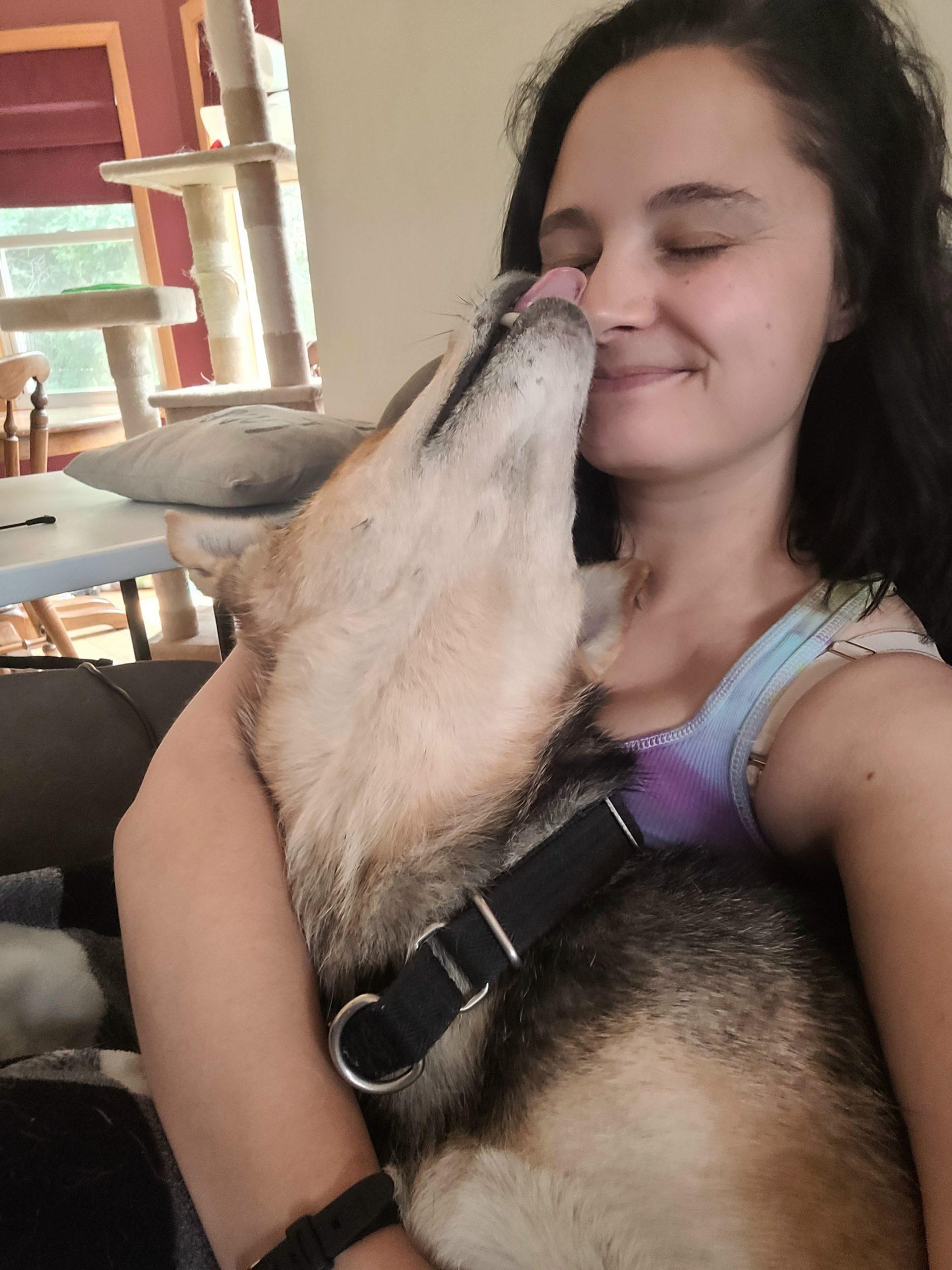 A woman takes a selfie while a big dog licks her nose.
