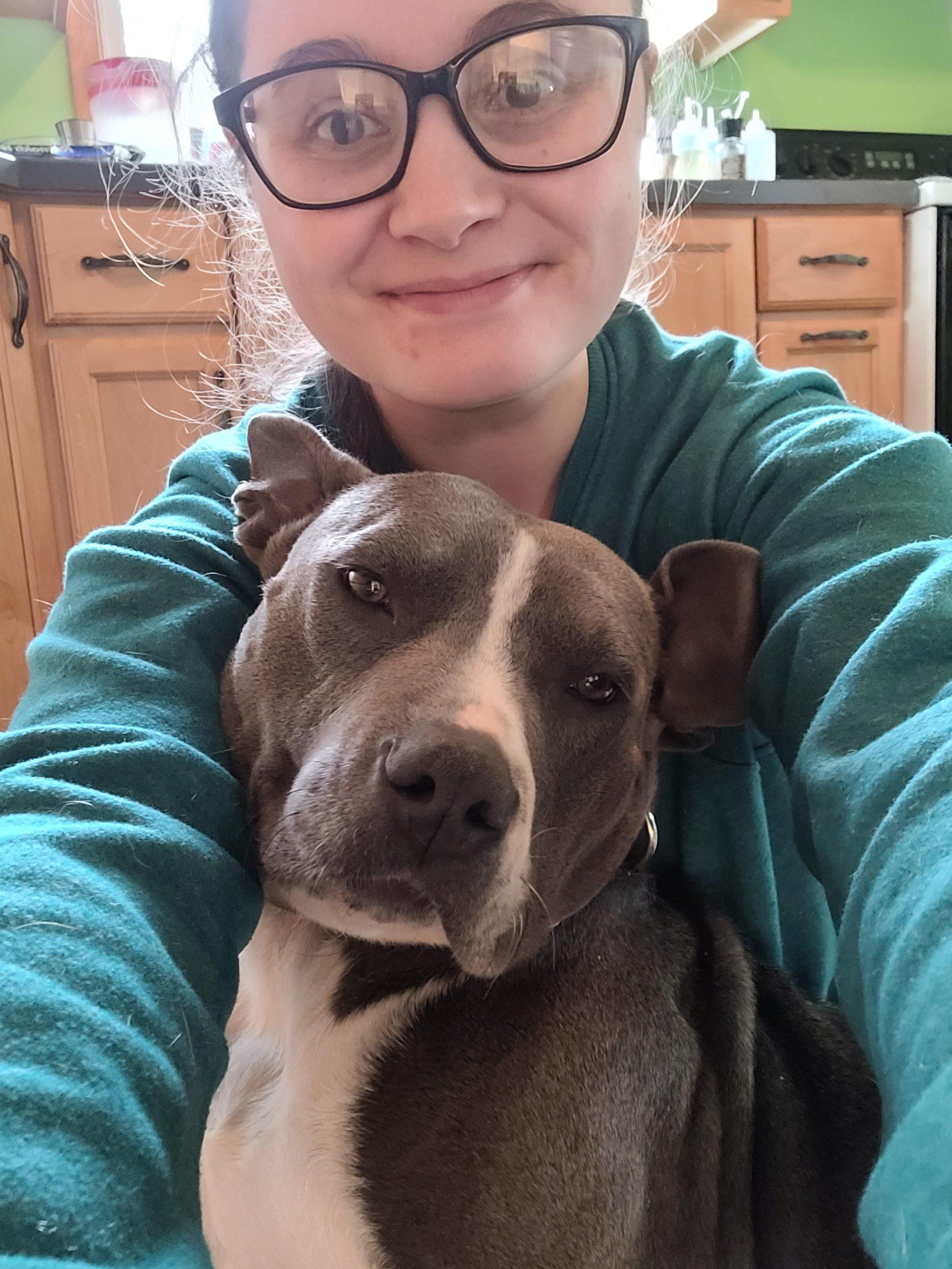 A woman takes a selfie with a grey and white dog.