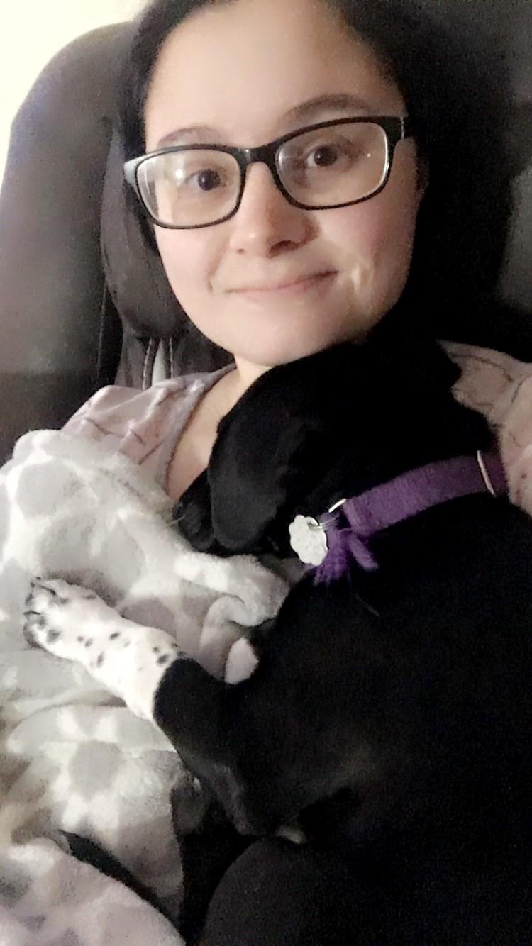 A woman poses with a black puppy asleep on her chest.