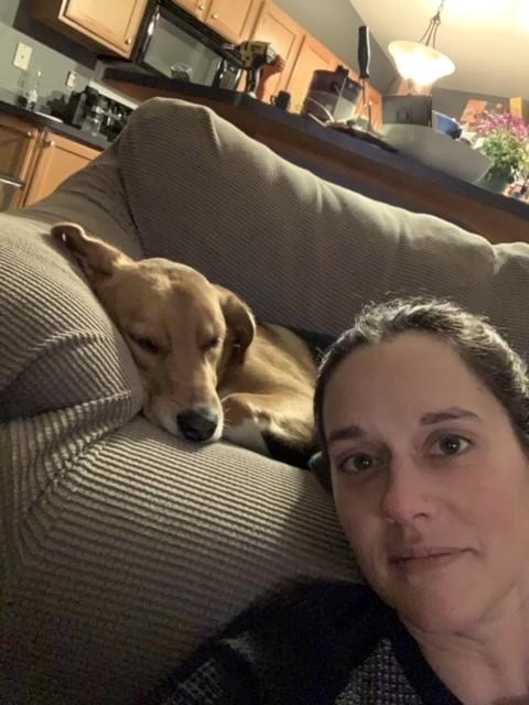 A woman poses with a brown dog asleep on the couch.