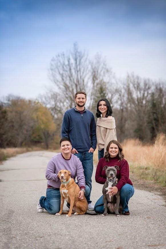 Four adults pose outside with two big dogs.